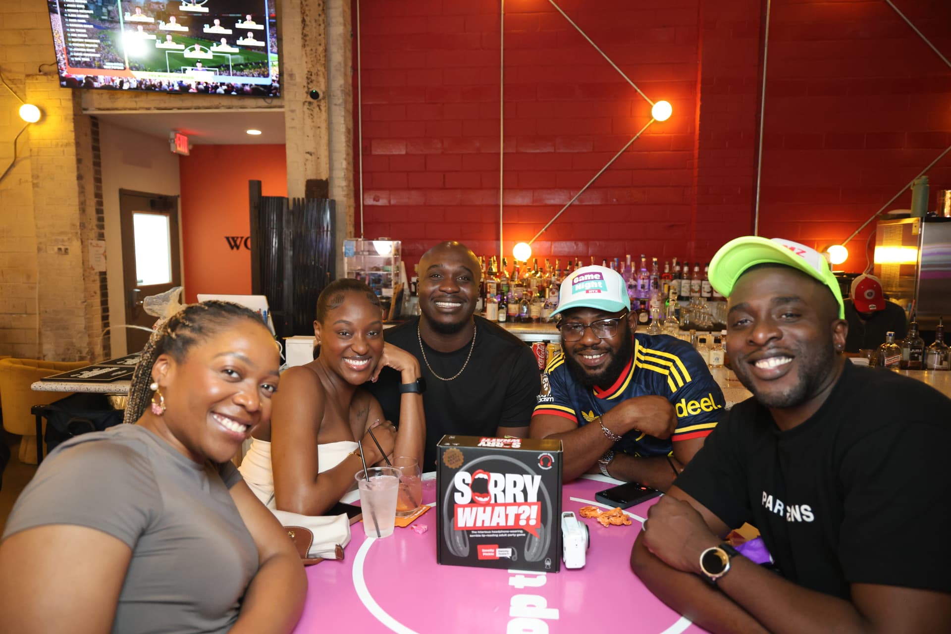 Five friends playing a party game around a pink table